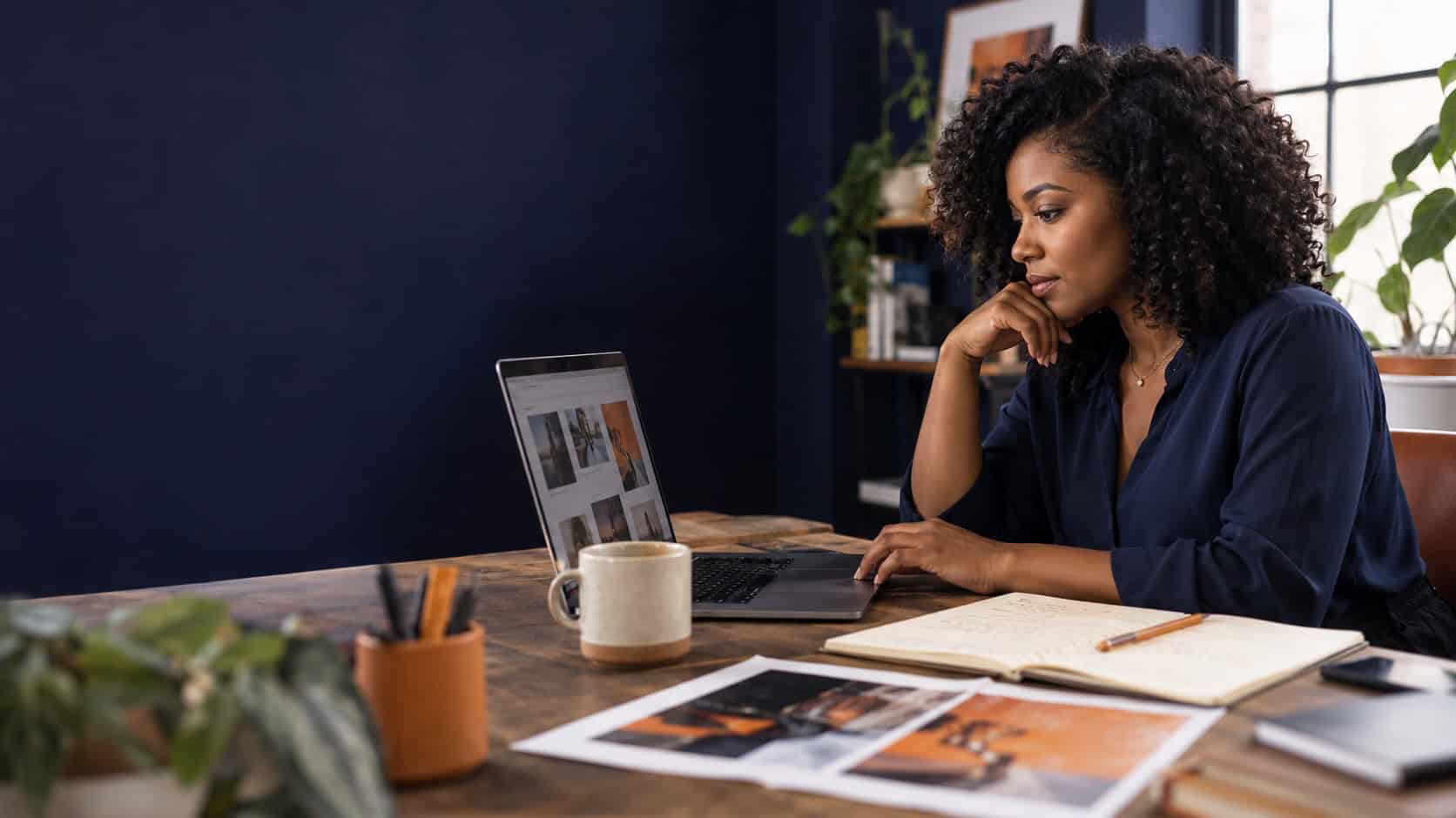 Woman reviewing advertising creative on a laptop beside handwritten notes and printed campaign concepts.